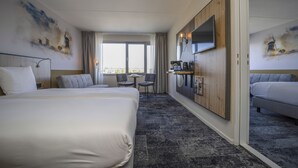 Een hotelkamer met twee bedden, een bureau, stoelen, een televisie en kunstwerken aan de muur.