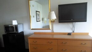 A hotel room with a wooden dresser, a television mounted on the wall, a microwave on a small table, and a lamp. - Yakima Valley Inn (Yakima)