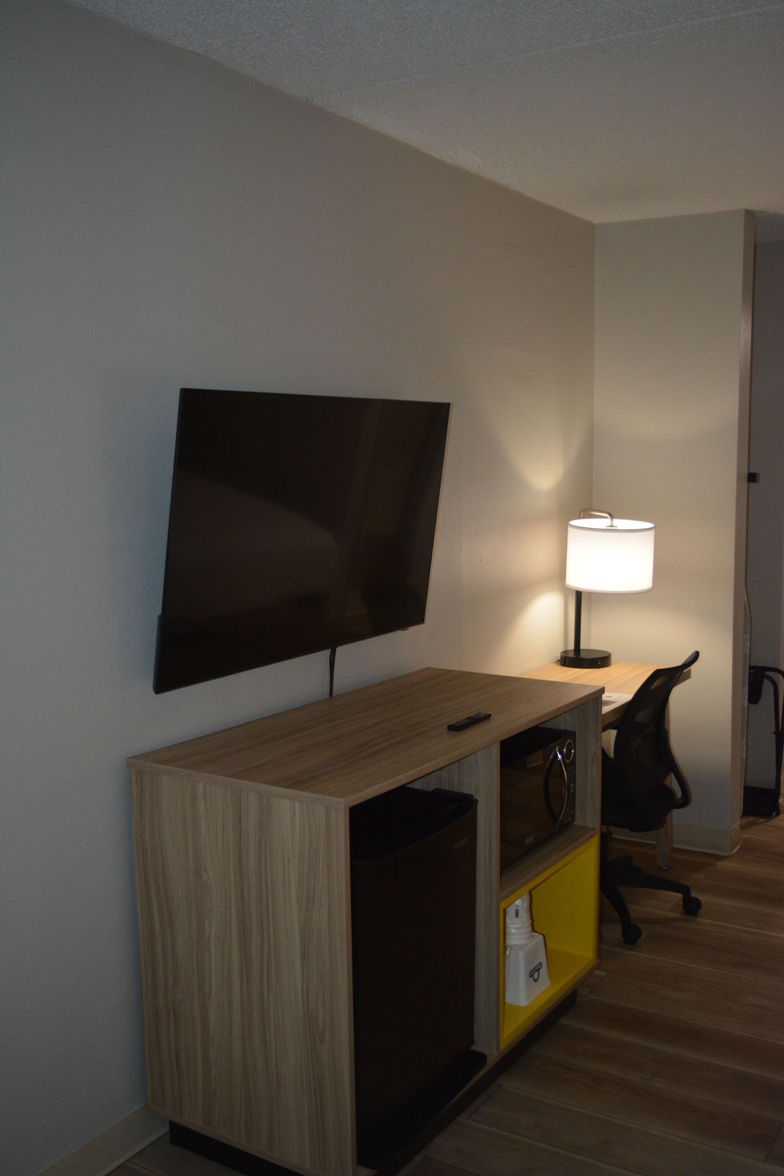 Habitació d'hotel amb televisió de pantalla plana penjada a la paret, escriptori amb làmpada, cadira i petit armari.