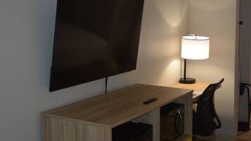 Habitació d'hotel amb televisió de pantalla plana penjada a la paret, escriptori amb làmpada, cadira i petit armari.