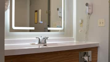 A bathroom with a large mirror, a sink, a hairdryer, and a trash bin.