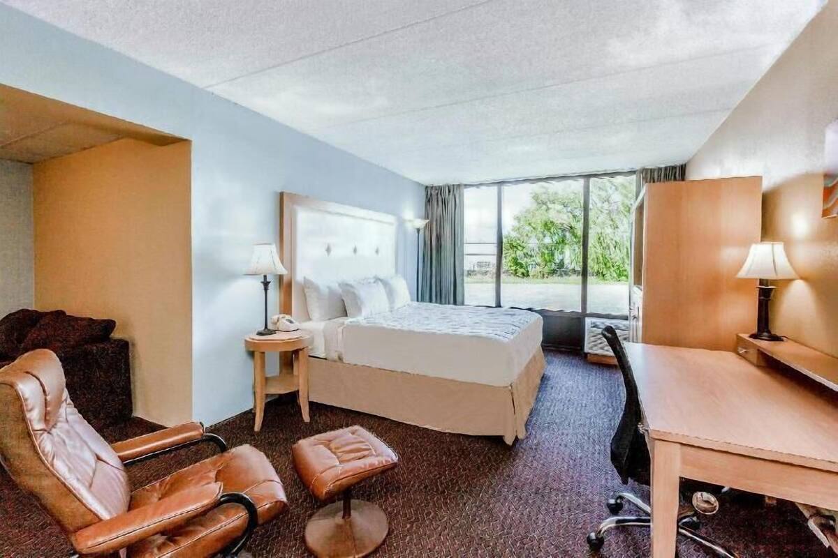 A hotel room with a bed, a desk, a chair, a small table, and a nightstand.