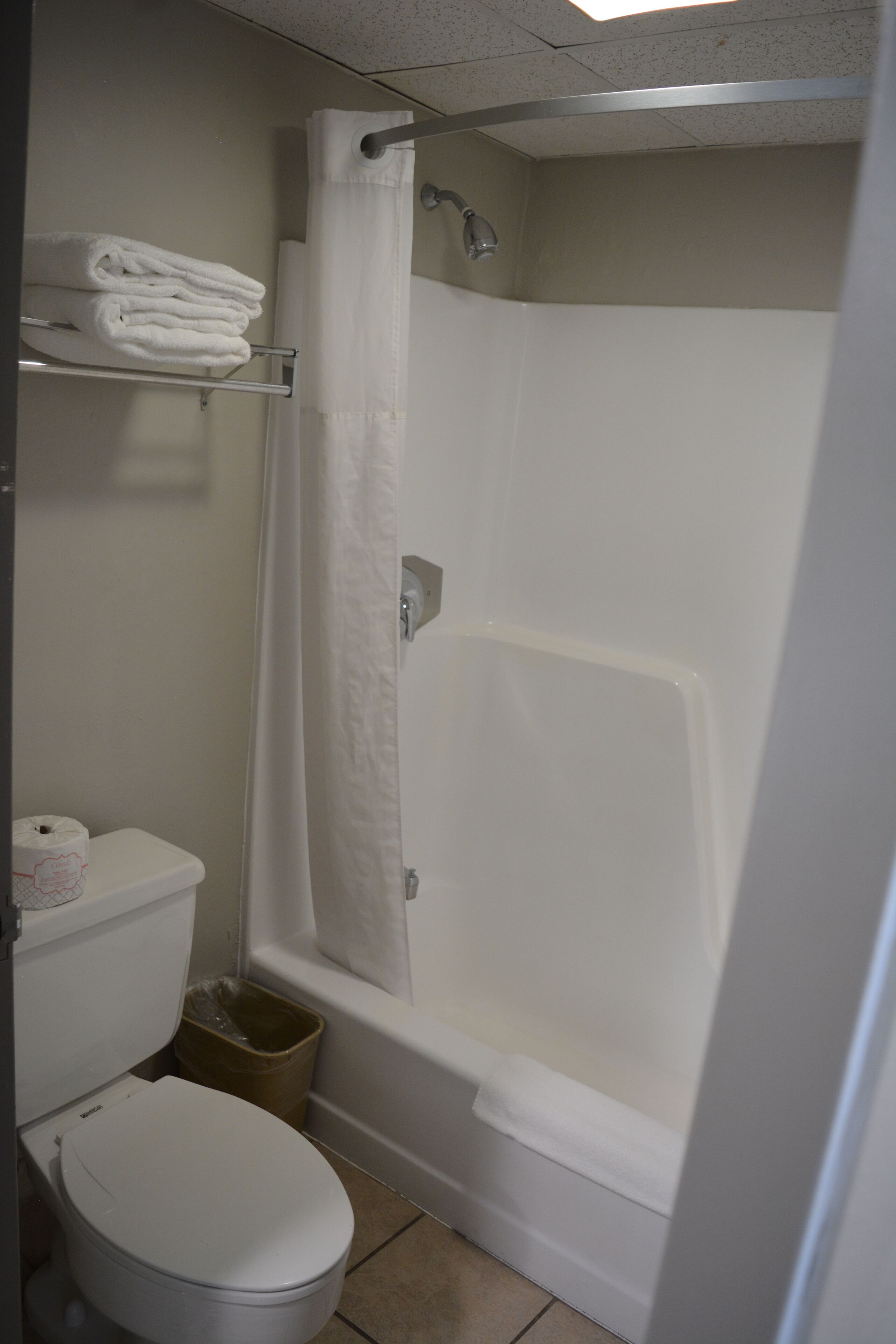A bathroom with a toilet, a shower with a curtain, and a shelf with folded towels.