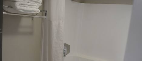 A bathroom with a toilet, a shower with a curtain, and a shelf with folded towels.