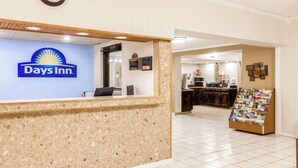A reception area with a Days Inn sign, a reception desk, a clock, and a display of magazines. - Days Inn by Wyndham Syracuse (Syracuse)