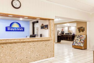 Zona de recepción con letrero de Days Inn, mostrador de recepción, un reloj y una exhibición de revistas.