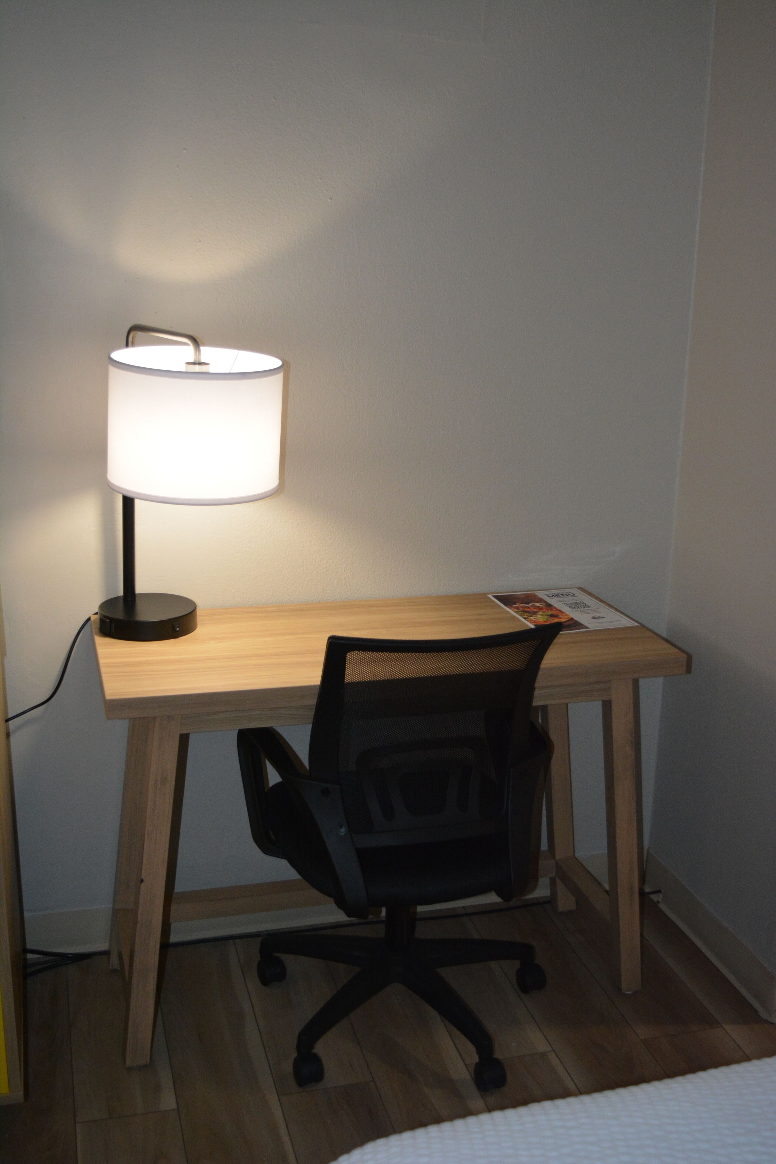 A wooden desk with a black office chair, a lamp, and a brochure on the table.