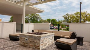 An outdoor patio with a stone fire feature, cushioned seating, and a covered area. - SpringHill Suites by Marriott Beaufort (Beaufort)