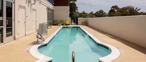 A swimming pool with a curved edge, a metal handrail, and a tiled deck.