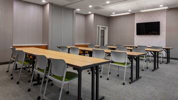 Une salle de conférence équipée de plusieurs tables et chaises, d’un téléviseur à écran plat fixé au mur et d’une porte dotée d’un appareil de climatisation.