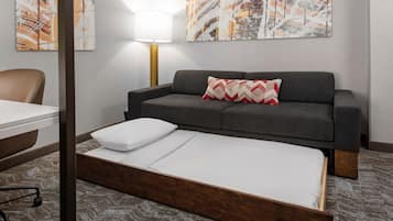 Ein Zimmer mit einem Bett, einem grauen Sofa, einem Schreibtisch und einer Lampe.