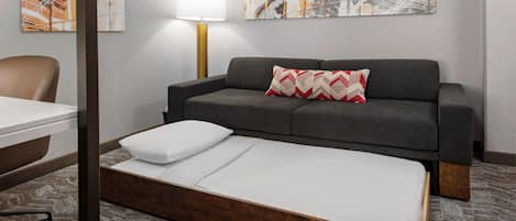 Ein Zimmer mit einem Bett, einem grauen Sofa, einem Schreibtisch und einer Lampe.