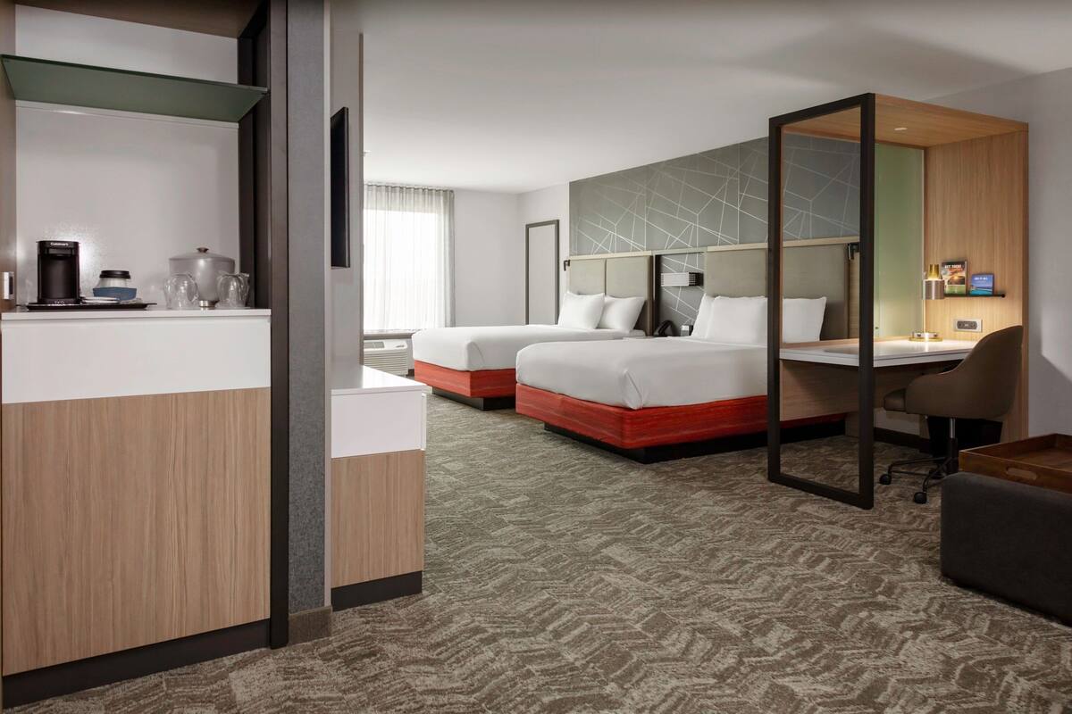 A hotel room with two beds, a desk, and a kitchenette.