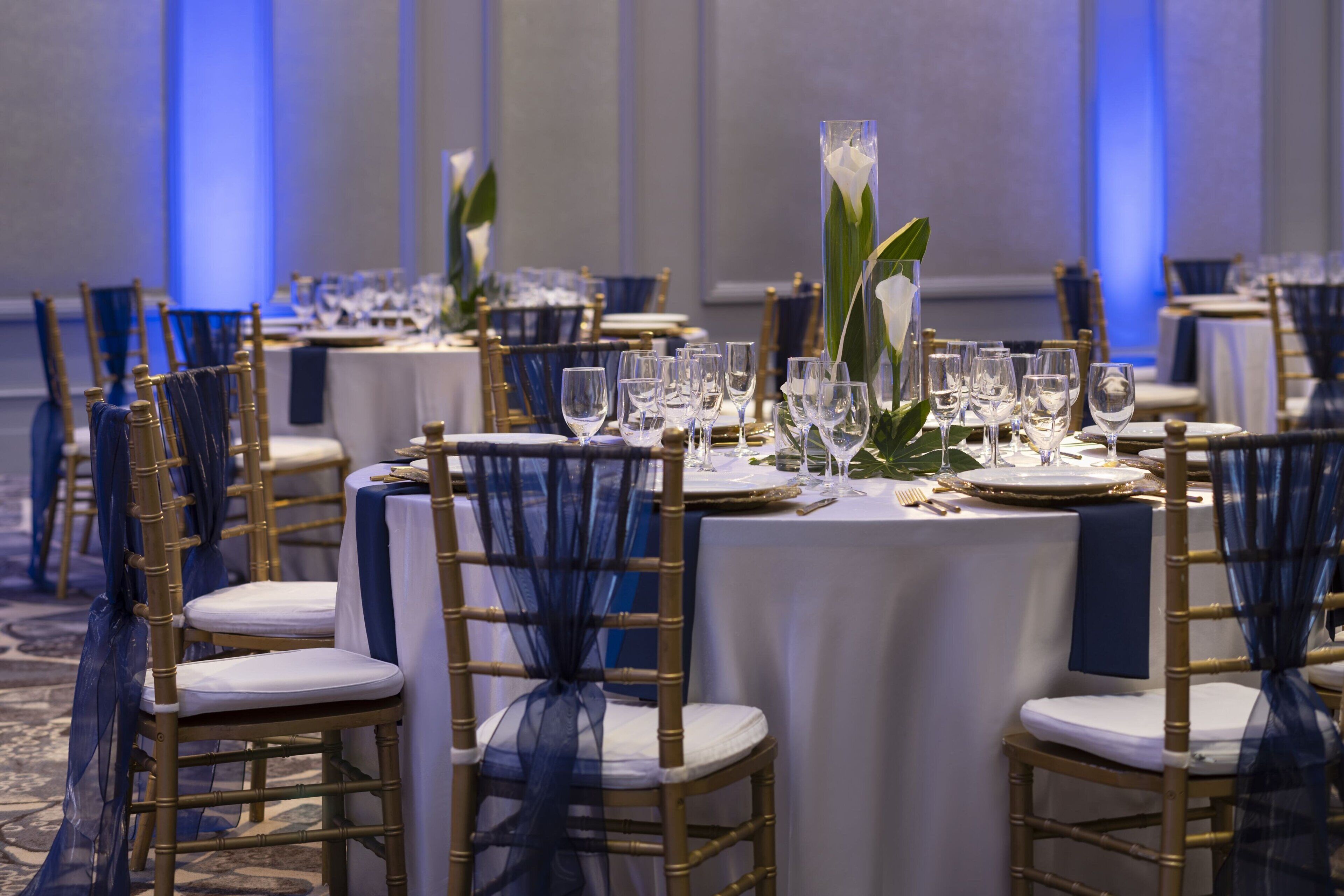 A banquet hall with round tables set for dining, featuring gold chairs and white tablecloths.