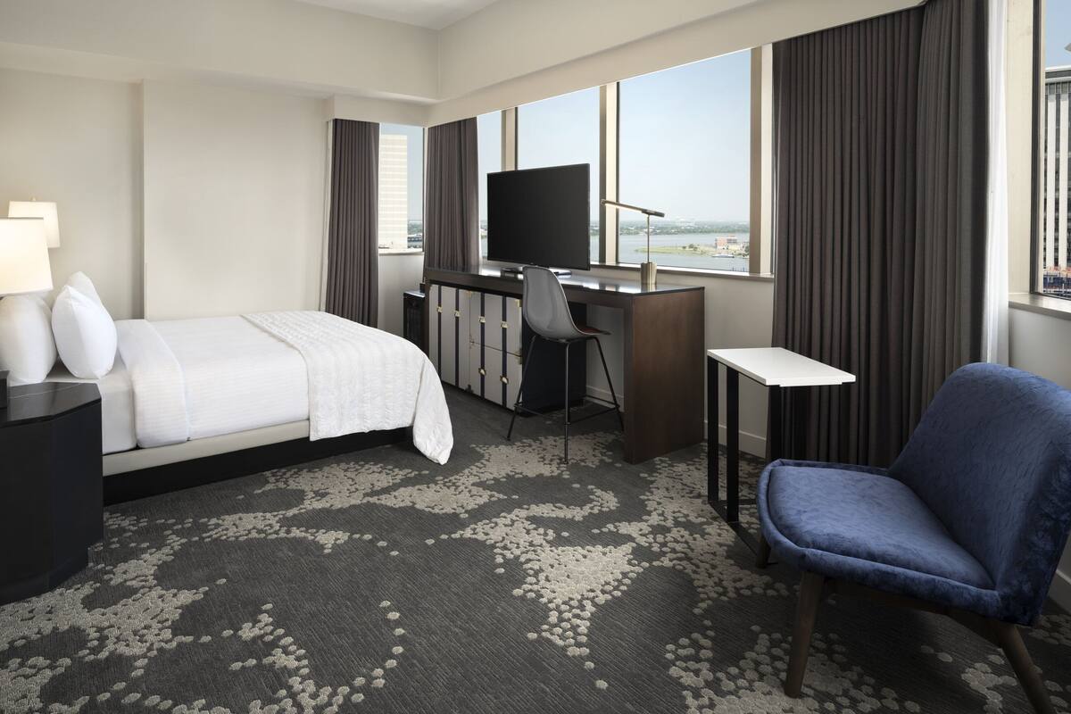 Ein Hotelzimmer mit Bett, Schreibtisch, Stuhl, Fernseher und großen Fenstern mit Blick.