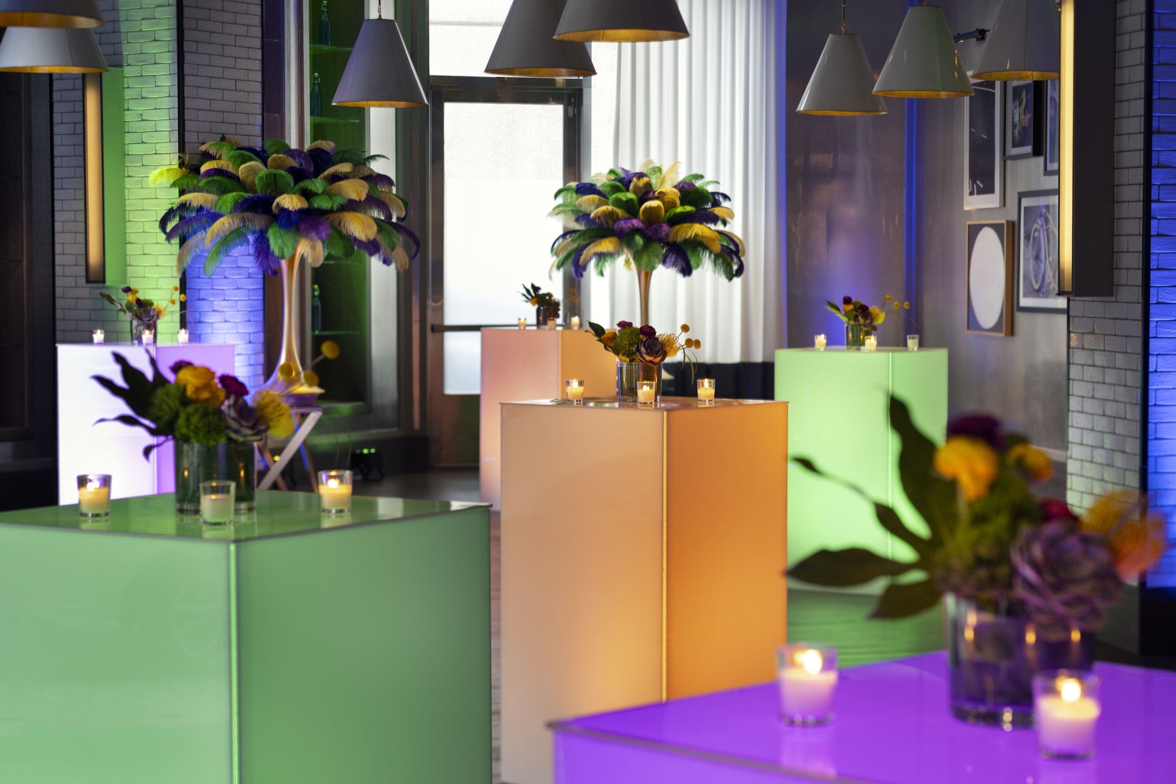 Een moderne hotellobby met groen en paars licht, decoratieve vazen met bloemen en een met baksteen beklede muur.