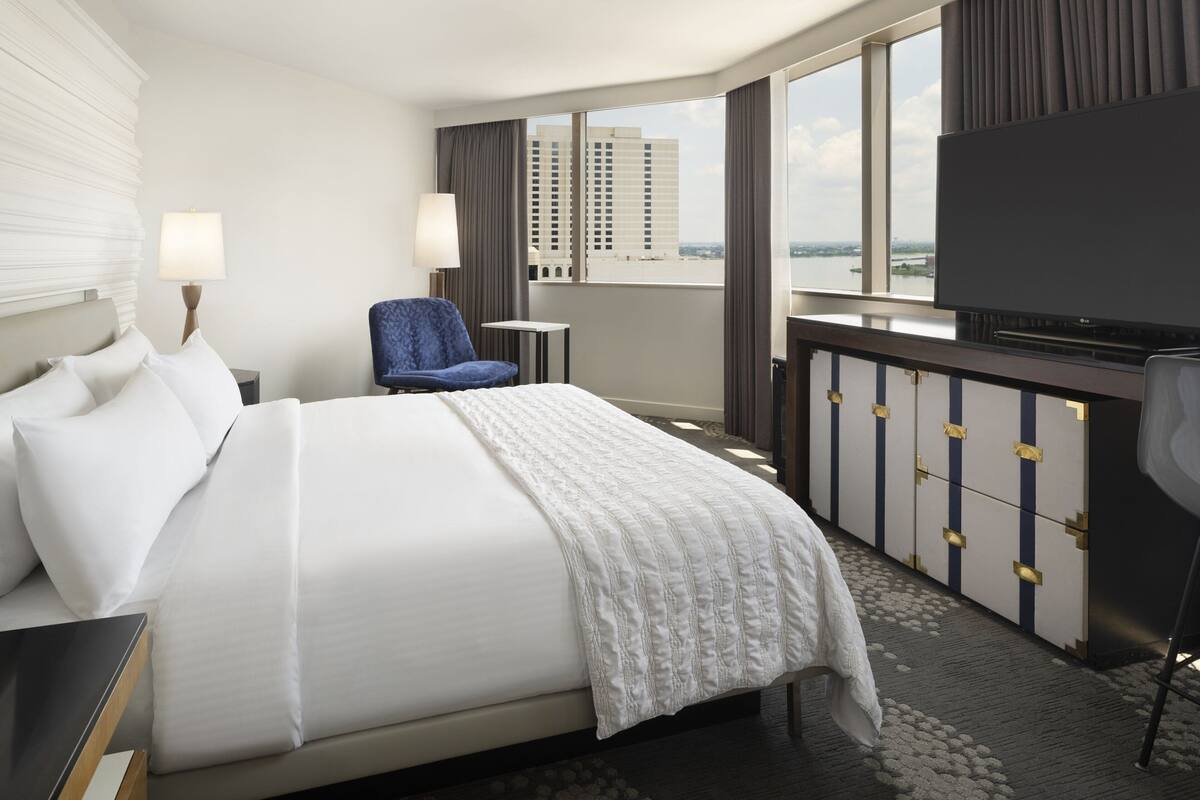 Ein Hotelzimmer mit einem großen Bett, einem Fernseher, einem Sessel und Blick auf die Stadt.