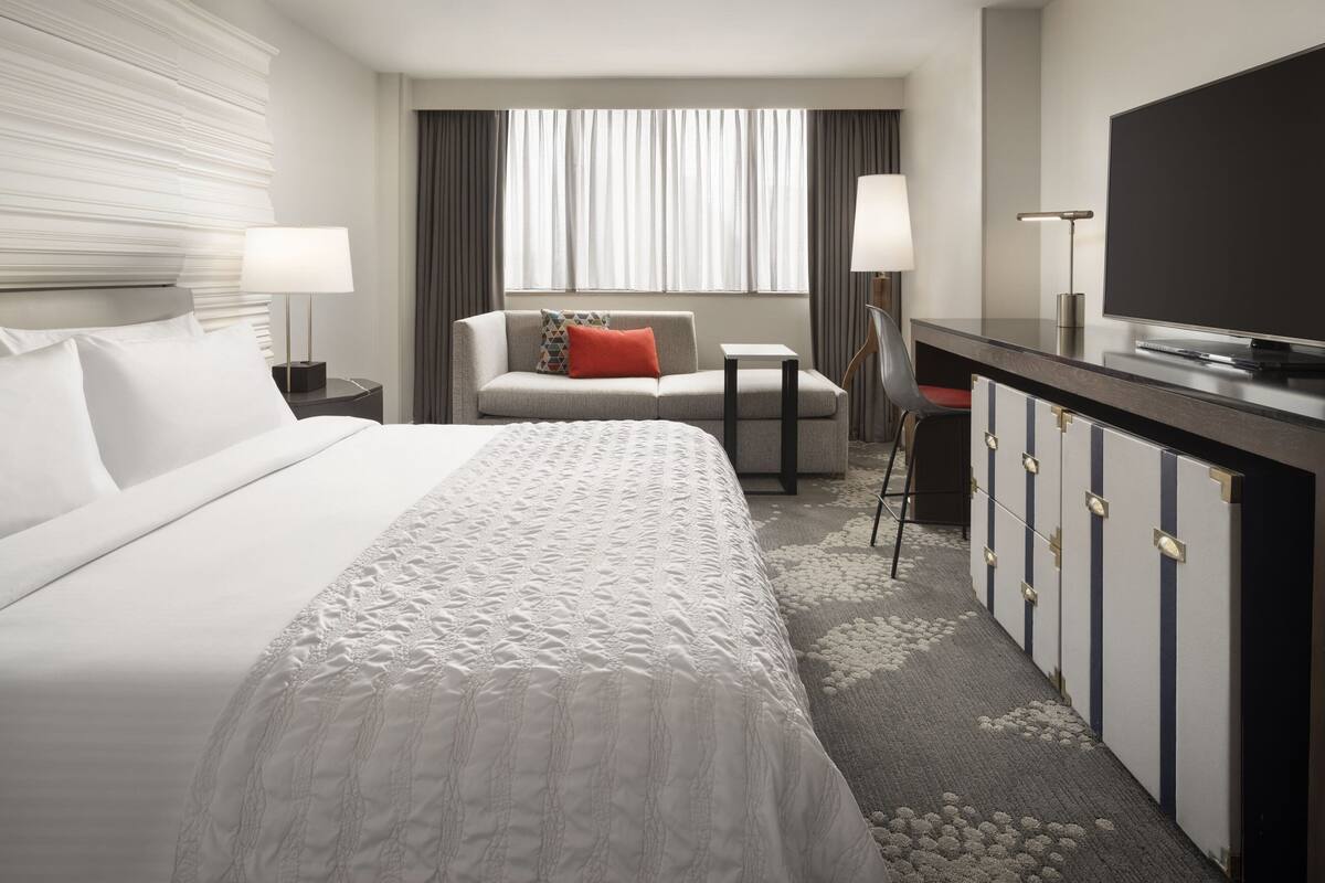 Ein Hotelzimmer mit einem großen Bett, einem Schreibtisch mit Flachbildfernseher, einer Couch und einem Sessel.