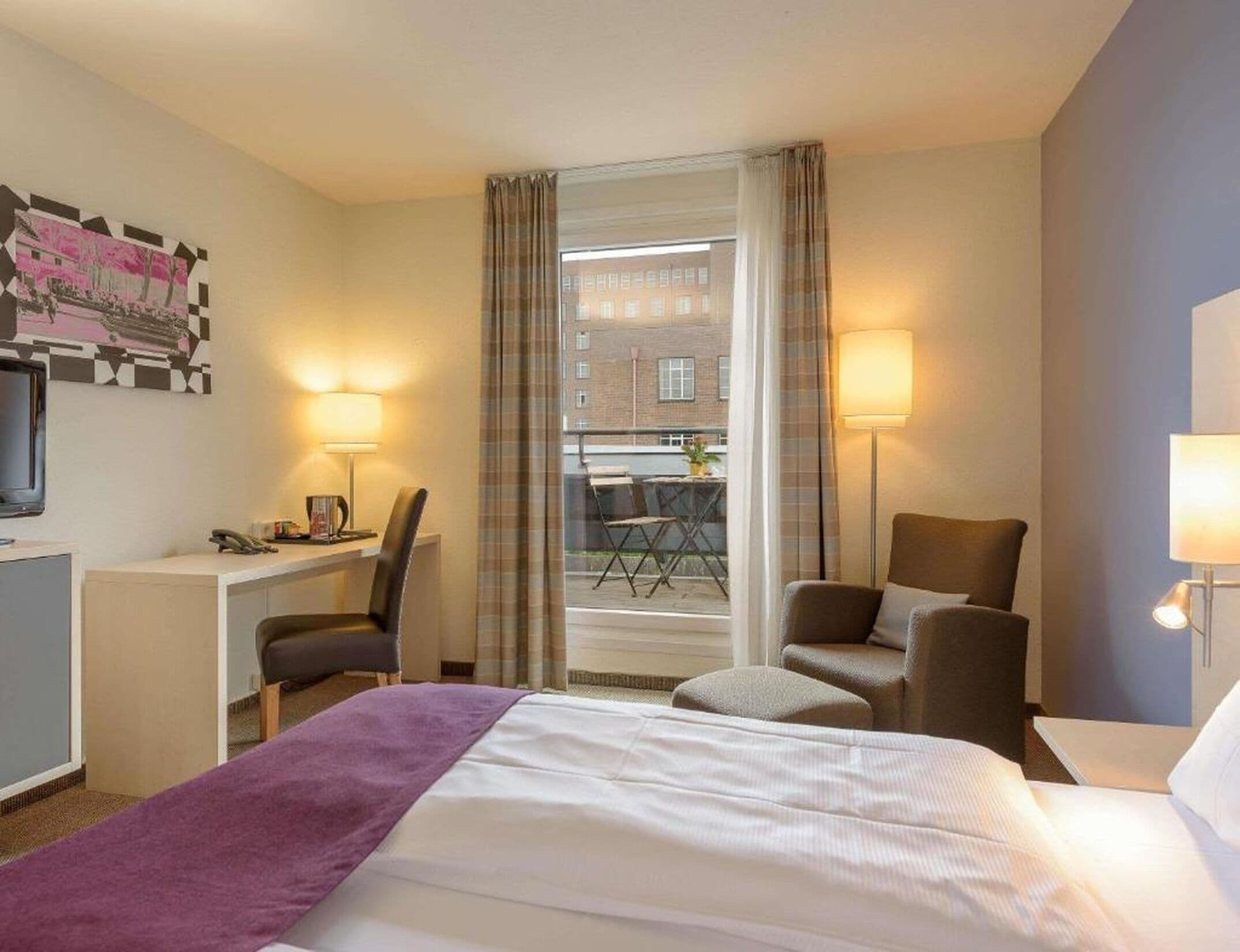 A hotel room with a bed, desk, chair, and two lamps.