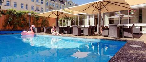 A swimming pool with lounge chairs and umbrellas, surrounded by buildings.