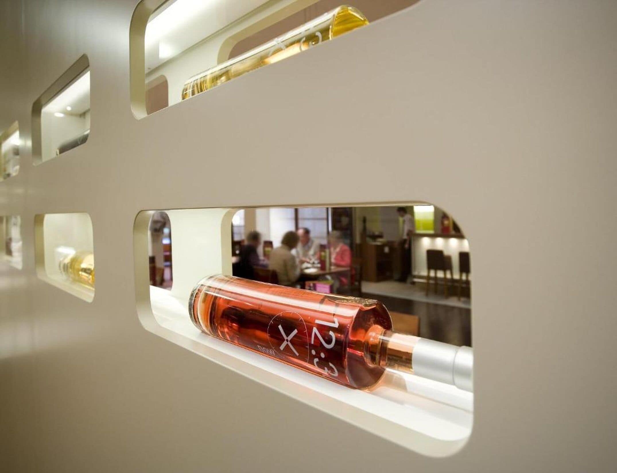 En cylinderformet genstand med en reflekterende overflade, muligvis en flaske, udstillet i en glasbeholder med reflekterende inderside.