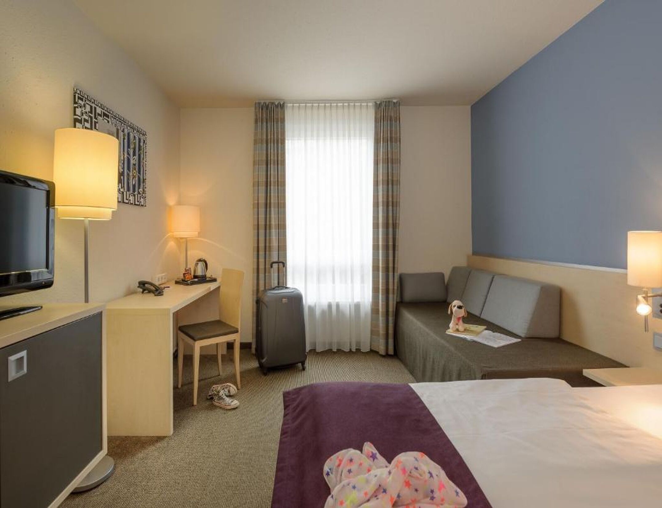 A hotel room with a bed, desk, chair, and a small sofa.