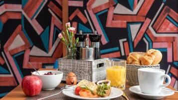 A breakfast setting with a plate of food, a glass of orange juice, a cup, a basket of bread, and a decorative vase with flowers.