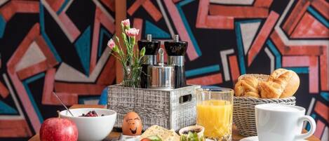 A breakfast setting with a plate of food, a glass of orange juice, a cup, a basket of bread, and a decorative vase with flowers.