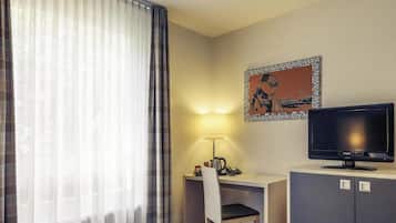 A hotel room with a bed, a desk with a chair, a television, a lamp, and a painting on the wall.