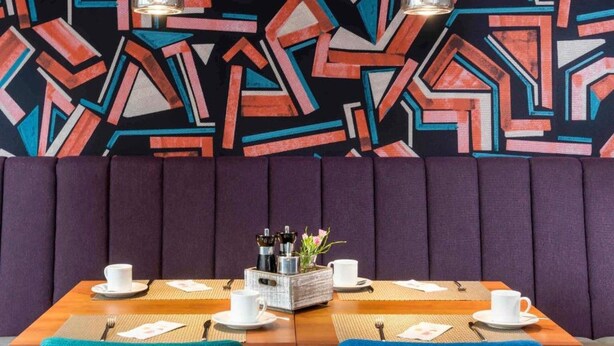 Comedor con pared de diseño geométrico, una mesa de madera y sillas azules.