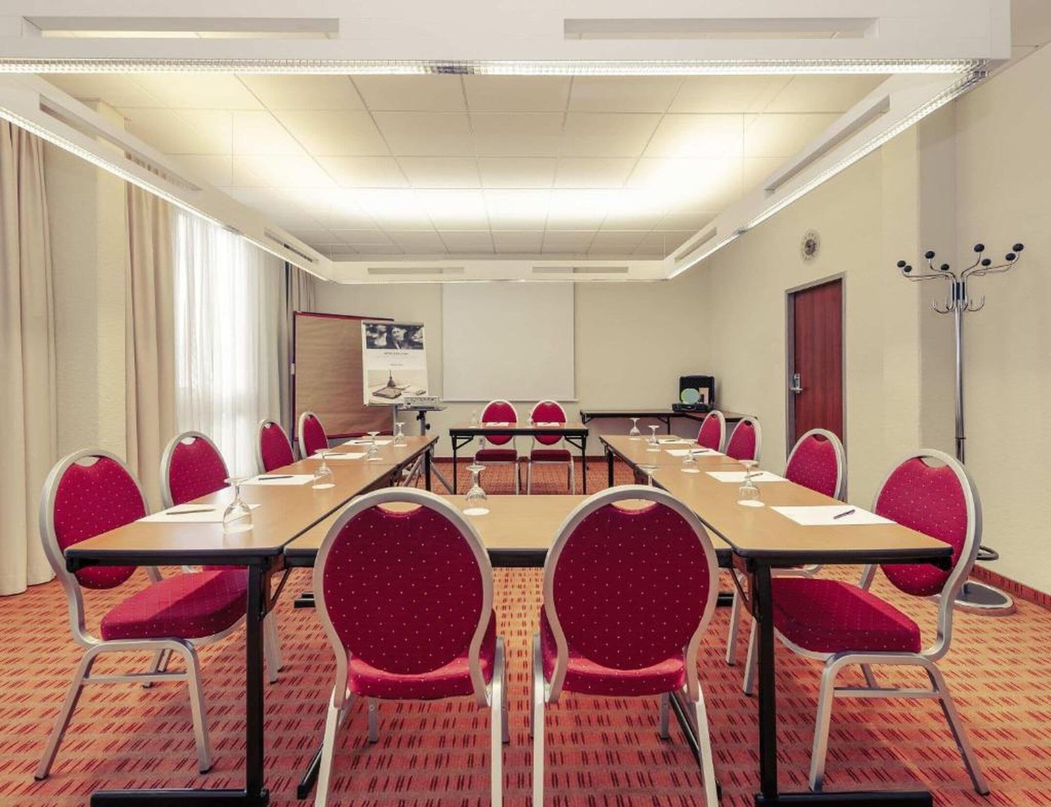 A conference room with a long table, red chairs, and a projector screen.