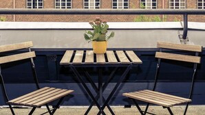 A rooftop terrace with a small table and two chairs, a potted plant, and a brick building in the background. - Sunday Hotel Berlin City West (Berlin)