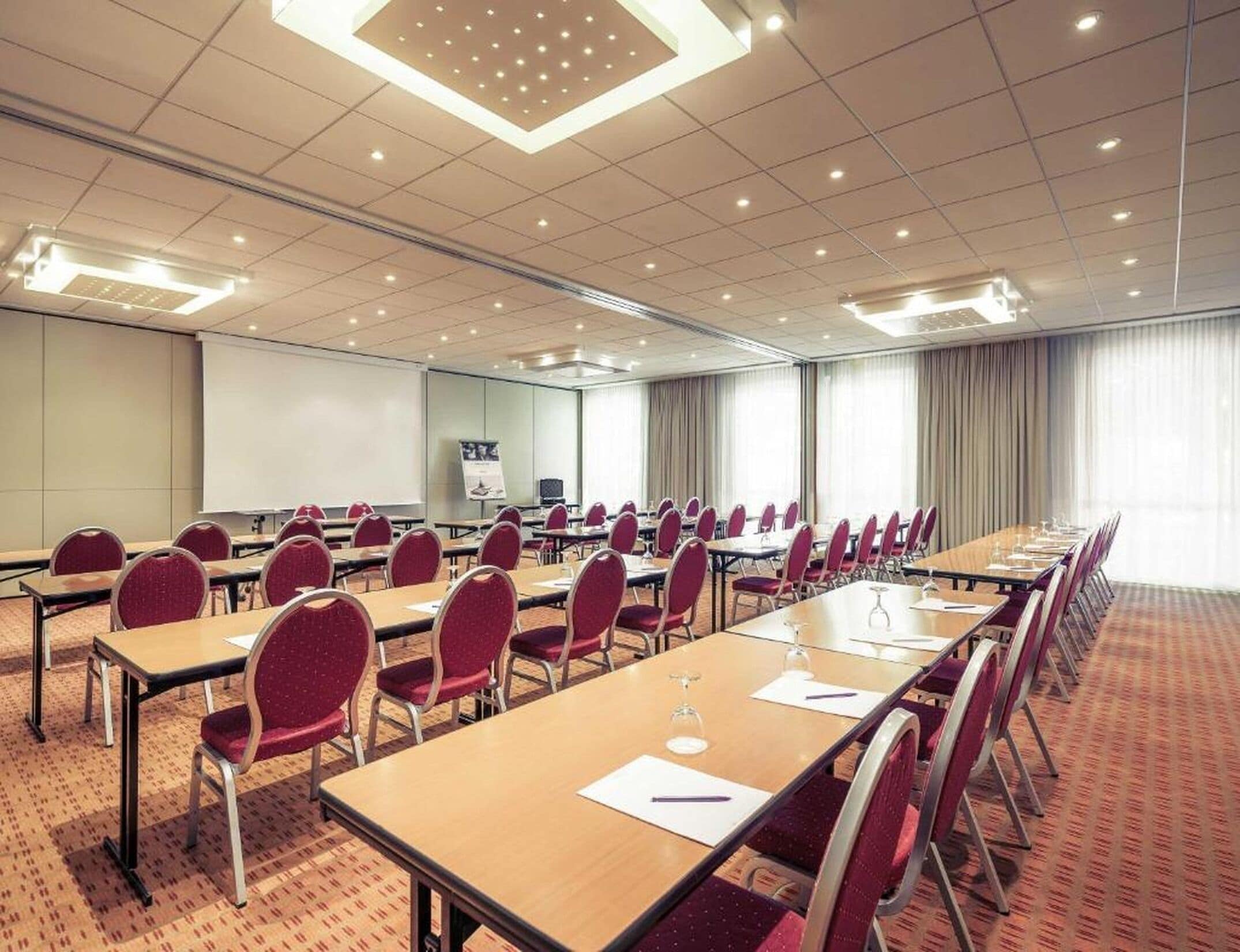 A conference room with multiple tables and chairs, a whiteboard, and a large window with curtains.