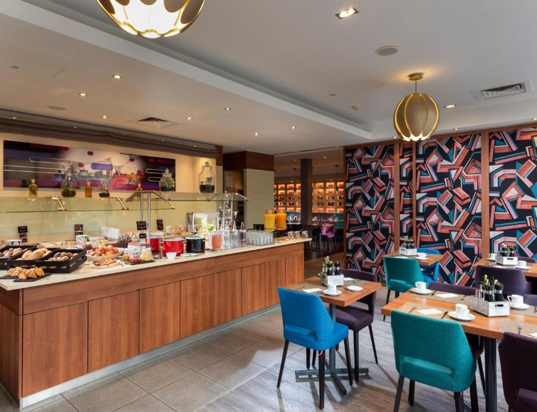 Ein modernes Restaurant mit einer zentralen Bar, Sitzgelegenheiten mit blau-violetten Stühlen und einer Wand mit Musterdesign.