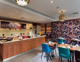 Un restaurante moderno con barra central, asientos con sillas azules y púrpuras, y una pared con diseño.