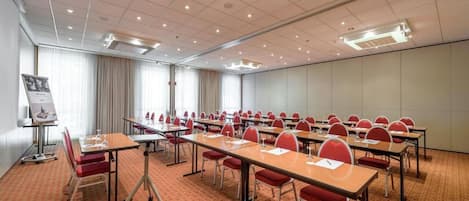 Una sala de conferencias con varias mesas y sillas, una pantalla para proyector y piso alfombrado.
