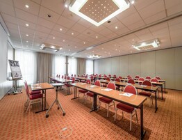 Una sala conferenze con diversi tavoli e sedie, uno schermo per proiettore e un pavimento rivestito di moquette.