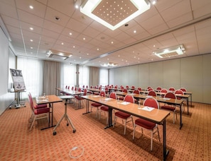 A conference room with multiple tables and chairs, a projector screen, and a carpeted floor. - Sunday Hotel Berlin City West (Berlin)