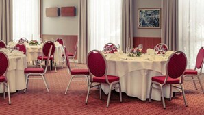 Un salón de conferencias con mesas redondas, sillas rojas y manteles blancos.