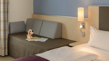 Habitación de hotel con cama, sofá, mesita de noche, lámpara y un pequeño peluche.