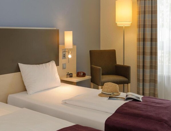 A hotel room with a bed, a chair, a nightstand, a lamp, and a window with curtains. - Sunday Hotel Berlin City West (Berlin)