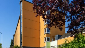 Un edificio moderno con fachada plana, varias ventanas y un área de estacionamiento con una camioneta blanca.