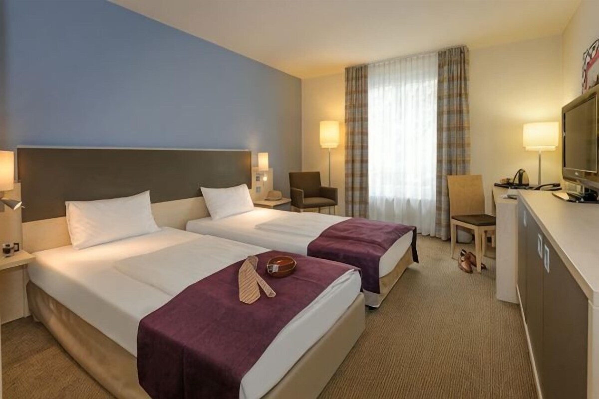 Habitación de hotel con dos camas, un escritorio, una silla y un televisor.