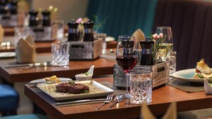 A restaurant setting with multiple tables, each with a plate of food, a glass of red wine, and a water glass. - Sunday Hotel Berlin City West (Berlin)