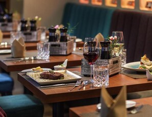 Un restaurante con varias mesas, cada una con un plato de comida, una copa de vino tinto y un vaso de agua.