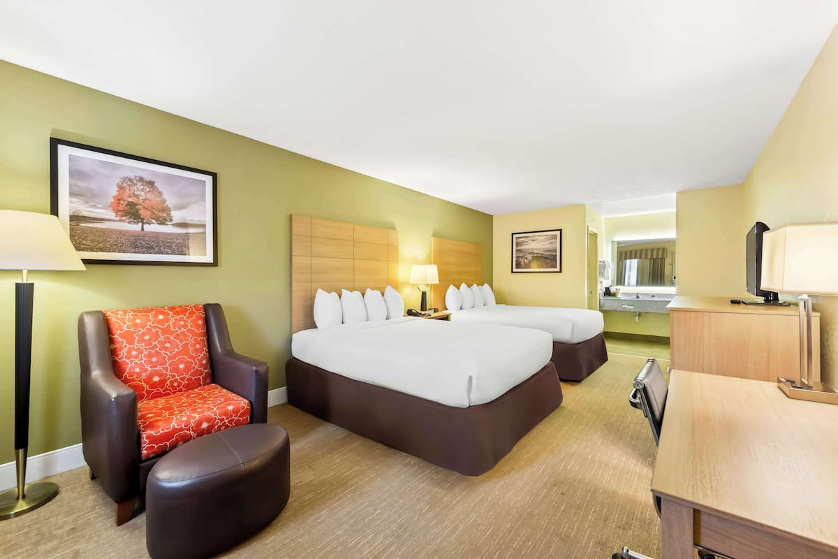 A hotel room with a bed, a chair, a desk, and a bathroom visible in the background.