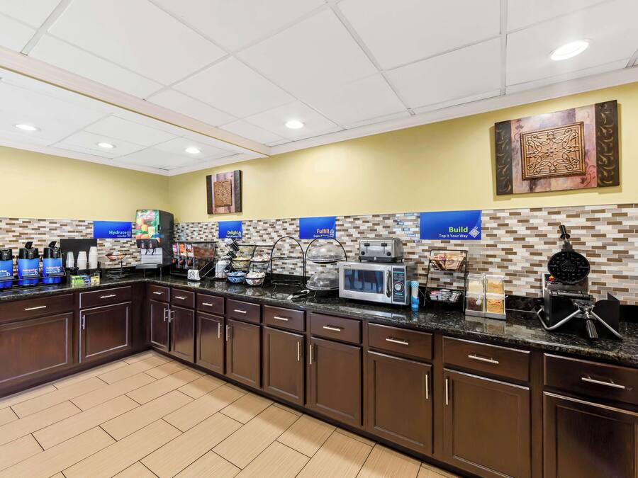 A hotel kitchen with a long counter, microwave, coffee maker, and various food items.