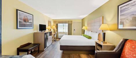 A hotel room with a bed, a desk, a chair, a sofa, a TV, and a bathroom with a bathtub.