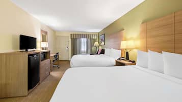 A hotel room with two beds, a desk with a TV, a mini-fridge, a lamp, and a nightstand.