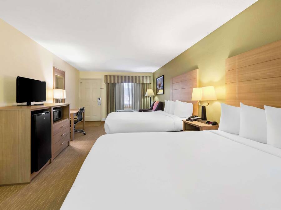 A hotel room with two beds, a desk with a TV, a mini-fridge, a lamp, and a nightstand.